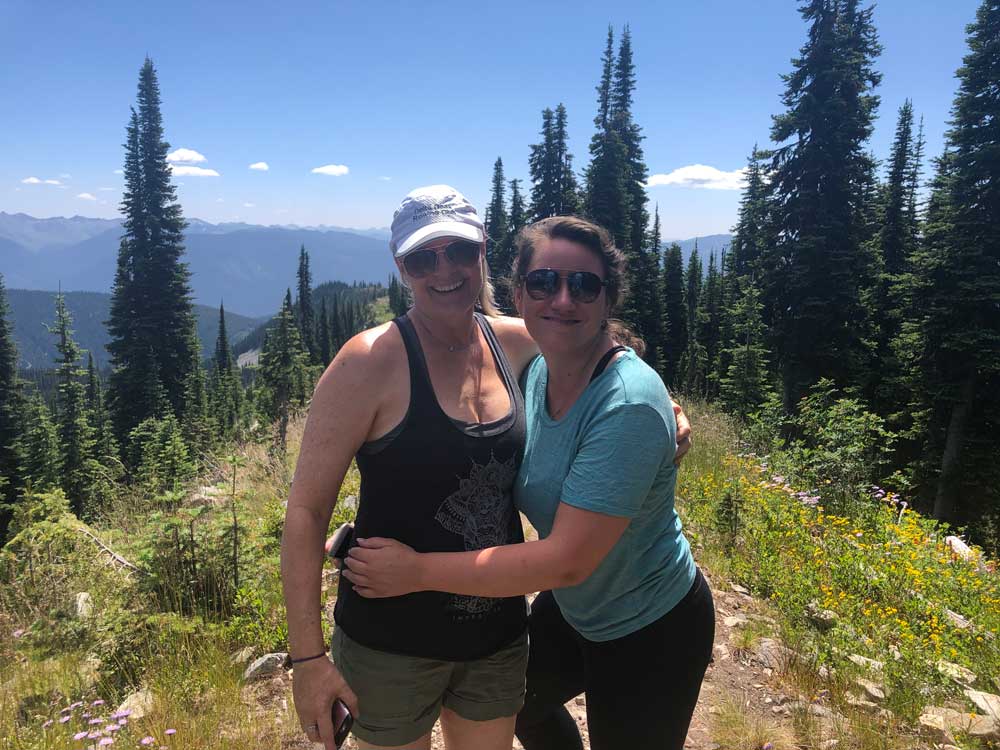connection between quality of life and health feature image, two girls hiking in the mountains, smiling and hugging, sunshine, massage therapy nelson